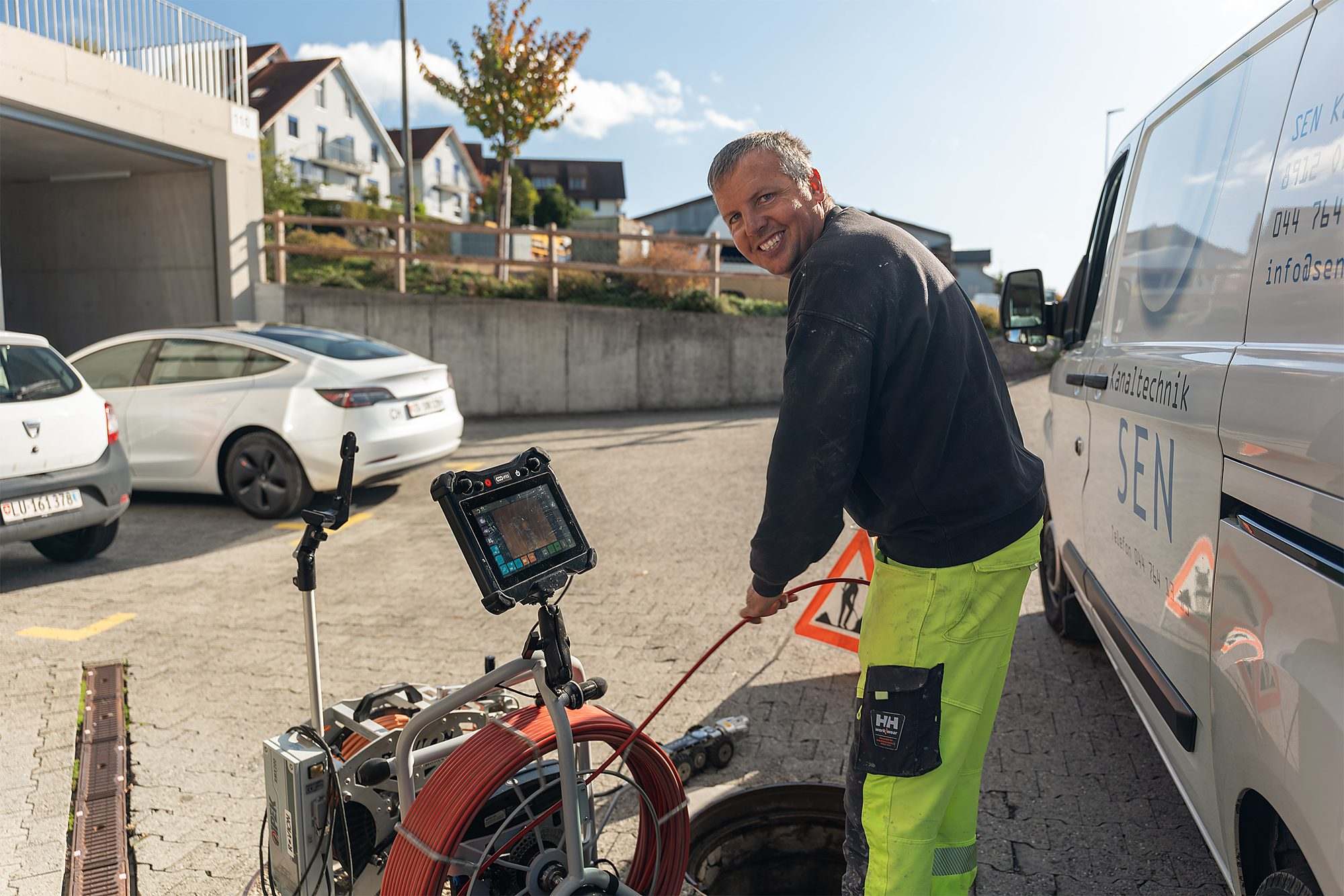 Mitarbeiter mit der Kanalkamera am offenen Schacht, auf dem Bildschirm das Bild aus der Leitung