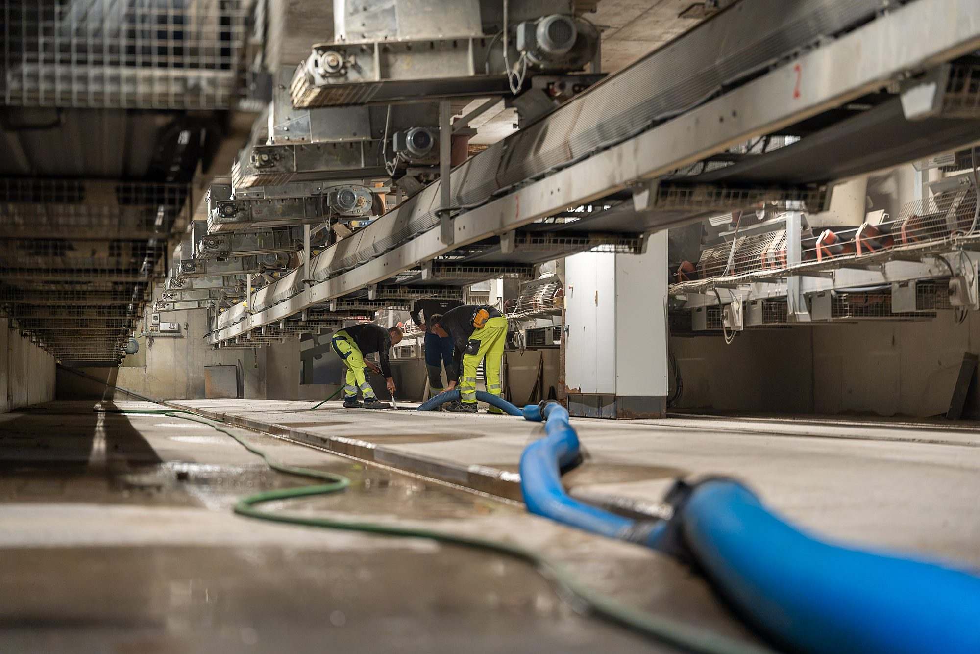 Saugschlauch in einem Becken einer Industrieanlage, im Hintergrund zwei Mitarbeiter