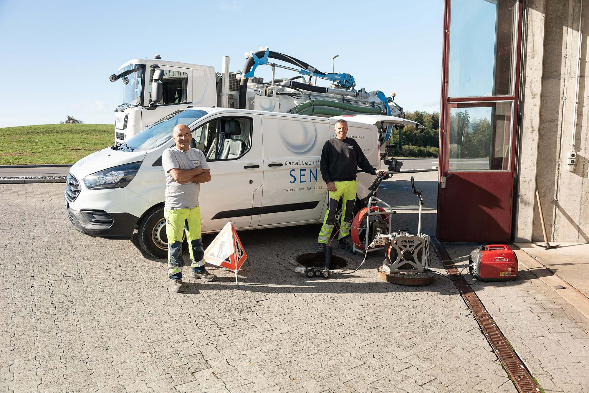 Zwei Mitarbeiter mit Servicefahrzeug, Saugwagen und Geräten am offenen Schacht