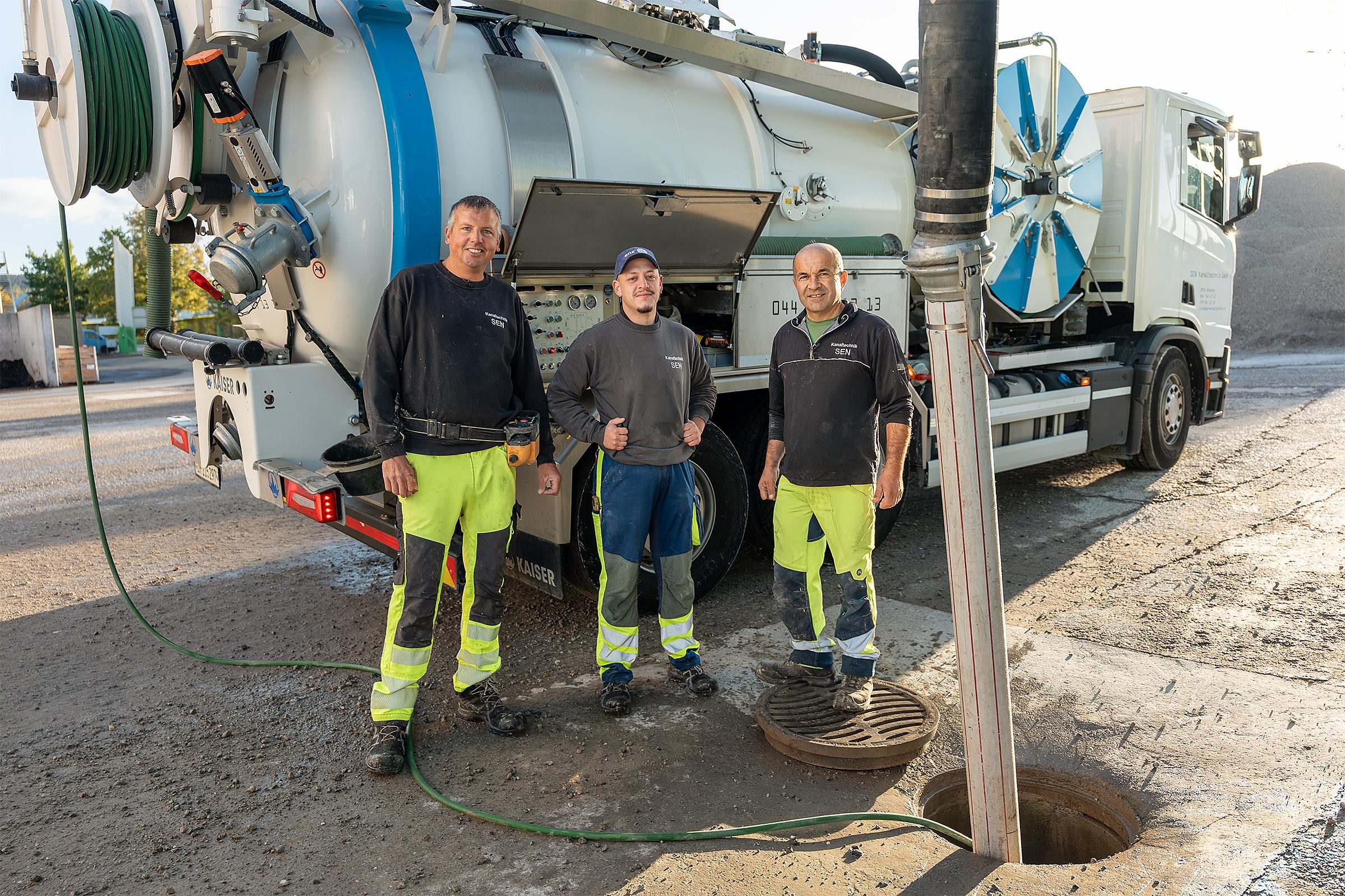 Drei Mitarbeiter der SEN Kanaltechnik am offenen Schacht vor dem Saugwagen